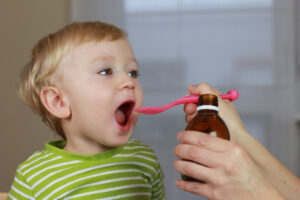 Mother giving 2 years old baby boy medicine, cough syrup on a spoon.